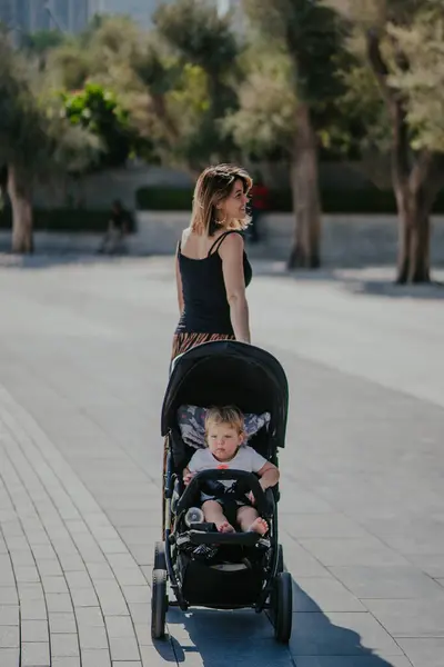 Dubai,  Unite dArab Emirates - October 19, 2019 - A woman is walking away from the camera, pushing a stroller with a young child inside, in an outdoor park setting.