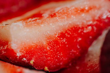 Yakın plan, canlı kırmızı renkli, buzla kaplı çilekler ve kısmen dilimlenmiş görünür tohumlar..