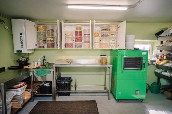 A well-organized garage space with a large green freeze-dryer, metal worktable, and cabinets filled with jars of freeze-dried fruits and supplies.
