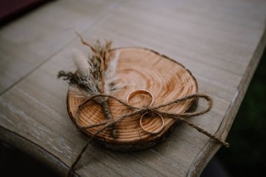 Valmiera, Letonya - 13 Ağustos 2023 - İki alyans ahşap bir levhada duruyor, sicimle bağlanmış, kurumuş çiçeklerle birlikte, bir düğünde birlik ve doğal zarafeti simgeliyor..