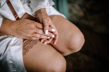 Valmiera, Letonya - 13 Ağustos 2023 - Kalçasında dinlenen, dantelli ve manikürlü tırnakları olan beyaz saten bir bornoz giyen bir kadının yakın çekimi.