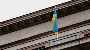 Riga, Letonya - 4 Nisan 2024 Mavi ve sarı bayrak klasik mimari detaylara sahip bir binaya karşı.