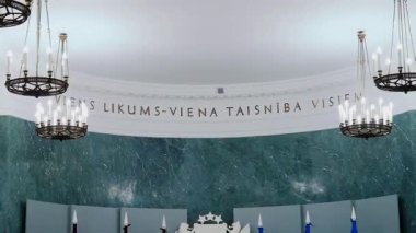 Riga, Letonya - 4 Nisan 2024 - İçinde kavisli bir yazı, avizeler ve mermer bir duvar olan zarif bir iç mekan. Metin büyük olasılıkla ulusal bir slogan veya ilke ifade ediyor.