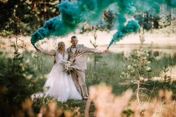 Bir gelin ve damat, ellerinde mavi sis bombalarıyla ormanda dikiliyorlar. Duman, olay yerine rüya gibi bir atmosfer katıyor..