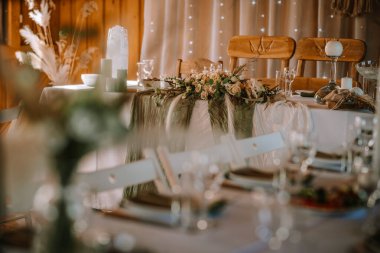 Valmiera, Letonya - 13 Ağustos 2023 - Çiçek süsü, mum ve ahşap sandalyeli zarif bir düğün masası.