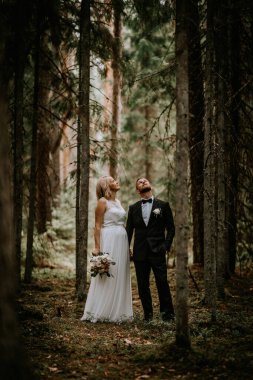 Valmiera, Letonya - 14 Temmuz 2023 - Bir gelin ve damat, yüksek çam ağaçlarının arasında dikilip etraflarındaki doğanın güzelliğini düşünürler..