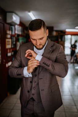 Valmiera, Letonya - 28 Temmuz 2024 - Özel dikim kahverengi takım elbiseli bir adam kol düğmelerini ayarlıyor, odaklanmış ve titiz bir tavırla önemli bir resmi olaya hazırlanıyor..