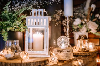 Valmiera, Letonya - 28 Temmuz 2024 - cam fenerlerin içinde mumların samimi bir düzenleme, parlayan ışıklar ve odun dilimlerinde yeşillik, sıcak, büyüleyici bir ortam yaratır.