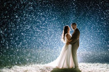 Valmiera, Letonya - 28 Temmuz 2023 - Bir gelin ve damat, arka planda parlayan yağmur damlalarıyla çevrili olarak bir araya gelir ve bokeh etkisi yaratır..