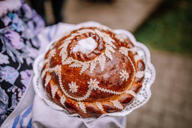 Valmiera, Letonya - 5 Ağustos 2023 - Çiçekli elbise giymiş birinin giydiği dantelli kumaş üzerindeki geleneksel bir ekmek, misafirperverliği ve kutlamaları simgeliyor..