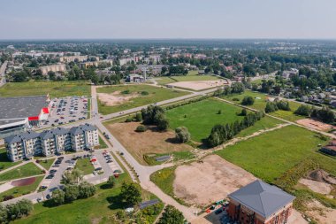 Valmiera, Letonya - 7 Ağustos 2023 - Konut binaları, büyük bir otopark, yeşil tarlalar ve ana yolu olan bir banliyö manzarası.