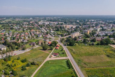 Valmiera, Letonya - 7 Ağustos 2023 - Evleri, bahçeleri, ana yolda bir kavşağı ve ağaçlarla çevrili yeşil arazileri olan bir yerleşim bölgesinin havadan görünüşü.