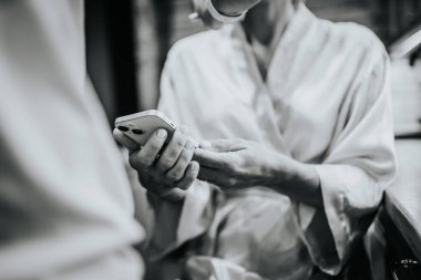 Valmiera, Letonya - 10 Ağustos 2023 - Beyaz cüppeli bir kişi ellerine odaklanmış akıllı telefon kullanıyor.