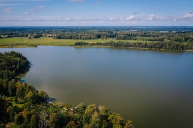 Valmiera, Letonya - 10 Ağustos 2023 - Açık bir günde çevresi orman ve tarlalarla çevrili büyük bir gölün havadan görünüşü.