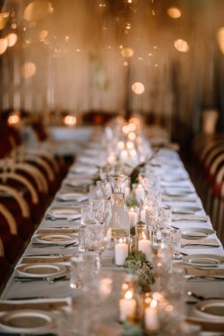 Valmiera, Letonya - 10 Ağustos 2023 - Arka planda muma, cama ve yeşilliğe sahip şık masa.