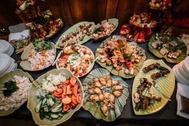 Valmiera, Letonya - 10 Ağustos 2023 - Bir dizi gurme yemekleri bir büfede, deniz ürünleri, salatalar, meyveler ve yeşil yaprak şekilli tabaklar üzerinde zarif bir şekilde düzenlenmiştir..