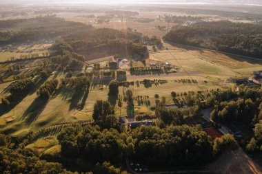 Valmiera, Latvia - August 12, 2023 - Sunlit aerial view of a 9-hole golf course with a driving range and surrounding forest. clipart