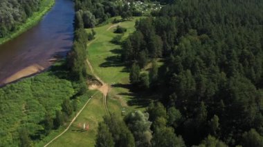 Valmiera, Letonya - 20 Ağustos 2023 - Ormandaki bir golf sahasının yanında uzanan bir nehrin havadan görünüşü, çimenlik alanlar, patikalar, ağaçlar, açık yaz günü.