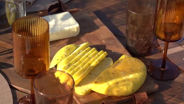 アンバーグラスとテーブルにワイングラスが付いた木製ボードのスライスチーズ — ストック動画