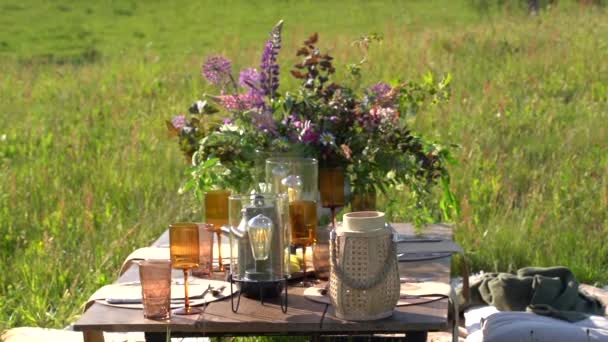 グラス ランタン 野生の花の花束を備えた屋外テーブルの設定 — ストック動画