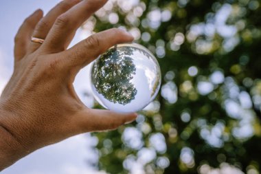Valmiera, Letonya - 19 Ağustos 2023 - Bir el, arka plandaki ağaçların ters çevrilmiş görüntüsünü yansıtan bir kristal küreyi tutuyor.