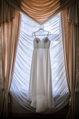 Valmiera, Letonya - 19 Ağustos 2023 - Zengin dekore edilmiş bir odanın penceresinin önünde asılı şık bir gelinlik.