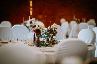 Valmiera, Letonya - 19 Ağustos 2023 - Süslü masaları, beyaz koltuk kılıfları ve kırmızı ve beyaz çiçeklerle süslü bir düğün salonu.