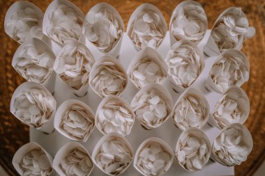 Valmiera, Letonya - 19 Ağustos 2023 - Masada sıra sıra dizilmiş beyaz çiçek yapraklarıyla dolu birçok beyaz kağıt koninin üst görüntüsü.