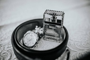 Valmiera, Letonya - 19 Ağustos 2023 - Siyah deri bir kemerin içinde zarif bir şekilde sergilenen lüks bir saat ve parfüm şişesi.