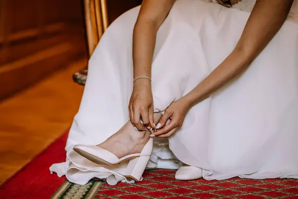 stock image Valmiera, Latvia - August 19, 2023 - Close-up of a bride sitting down, buckling her white wedding shoe on her foot, dressed in a beautiful white gown.