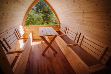 Ahşap bir kulübede, kemer penceresinin altındaki banklarla sade bir ahşap masa dışarıda yemyeşil bir manzara sunuyor..