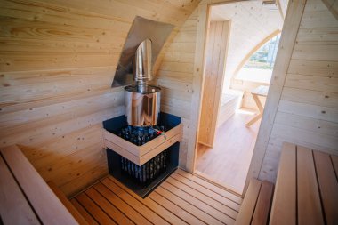 Küçük bir odada küçük bir bacası ve geniş bir penceresi olan kompakt bir sauna sobası olan ahşap bir kabinin iç manzarası..