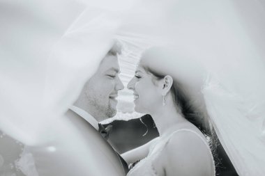 Valmiera, Letonya - 19 Ağustos 2023 - Bir gelin ve damadın yakın çekimi, yumuşak, akışkan kumaşla örtülü, samimi, rüya gibi bir atmosfer yaratıyor..