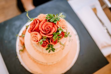 Valmiera, Letonya - 19 Ağustos 2023 - Kırmızı ve şeftali gülleriyle süslenmiş iki katlı bir pastanın üstü.