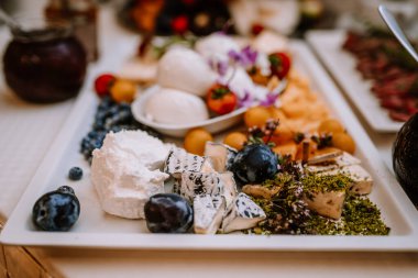 Valmiera, Letonya - 19 Ağustos 2023 - Açık büfe masasında çeşitli peynir, taze böğürtlen ve süslerin yer aldığı zarif bir peynir tabağının yakın çekimi.