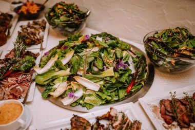 Valmiera, Letonya - 19 Ağustos 2023 - İçinde taze sebzeler ve yenilebilir çiçekler bulunan çeşitli salataların yer aldığı açık büfe masasının yakın çekimi.