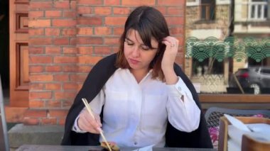 Bir kadın açık hava restoranında yemek çubuklarıyla suşi yiyor..