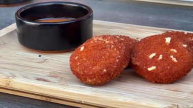 Sarımsakla süslenmiş, ahşap bir tahtada bir kase sosla servis edilen çıtır çıtır karidesli kekler..