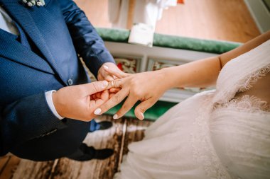 Valmiera, Letonya - 25 Ağustos 2023 - Gelin ve damadın nikah yüzüklerini değiş tokuş ederken, gelinin dantelli elbisesinin arka planına karşı ellerine odaklanan.