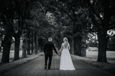 Valmiera, Letonya - 25 Ağustos 2023 - Bir gelin ve damat el ele yürür, sakin, siyah ve beyaz bir fotoğrafta yakalanır..