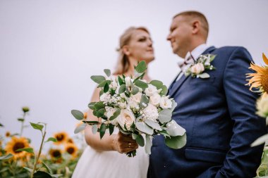 Valmiera, Letonya - 25 Ağustos 2023 - Gelin ve damadın el ele tutuşması, gelinin bir buket çiçek demeti ile yakın plan çekimi.