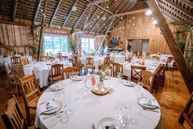 Valmiera, Latvia - August 25, 2023 - Rustic barn wedding reception setup with decorated tables and string lights. clipart