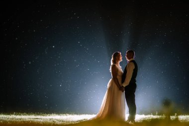 Valmiera, Letonya - 25 Ağustos 2023 - Bir çift yıldızlı gökyüzünün altında el ele duruyor, yüzen ışık lekeleriyle çevrili.