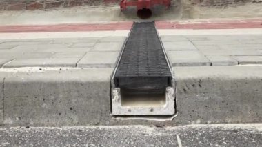 Şehir merkezinde verimli su boşaltma için tasarlanmış asfalt kaldırımlı bir kanalizasyon ve kaldırıma yakın çekim..