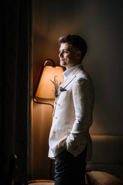 Riga, Letonya, - 26 Ağustos 2024 - lavantalı bej takım elbiseli adam pencereden dışarı bakar.