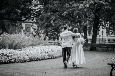 Riga, Letonya - 26 Ağustos 2024 Gelin ve damat bir park yolunda el ele yürüyorlar, arkadan bakıyorlar..