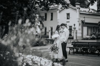 Riga, Letonya, - 26 Ağustos 2024 - Gelin ve damat parkta öpüşüyor, ön planda bulanık çiçekler var.