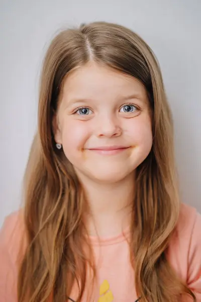 stock image A smiling young girl with long brown hair and blue eyes, wearing a peach-colored shirt and small heart-shaped earrings.