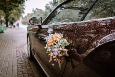 Riga, Letonya, - 26 Ağustos 2024 - Üzerinde çiçekler olan lüks bir araba, ıslak bir caddeye park edilmiş, üzerinde yağmur damlaları ve kaldırımlar olan, zarif ve romantik bir sahne..