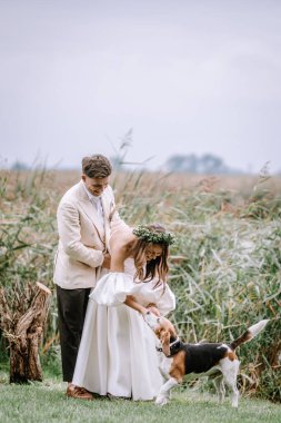 Riga, Latvia, - August 26, 2024 - a bride and groom are seen outdoors, enjoying a moment with their dog, symbolizing love and happiness.